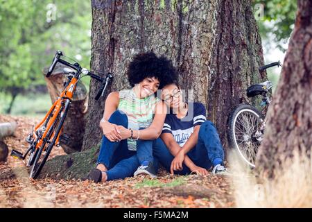 Reife Frau und Sohn sitzen gegen Parkbaum Stockfoto