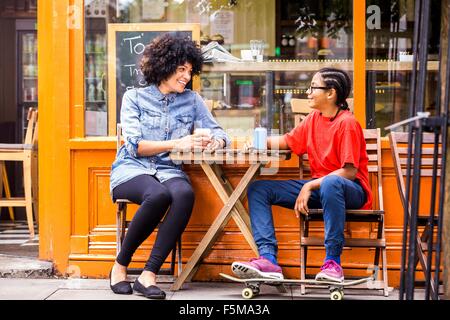 Skateboard Boy und Mutter am Straßencafé sitzen Stockfoto