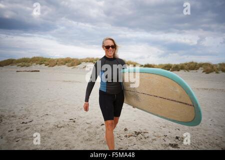 Ältere Frau zu Fuß am Strand, mit Surfbrett Stockfoto