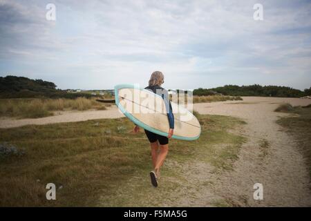 Ältere Frau zu Fuß entlang dem Strand, mit Surfbrett, Rückansicht Stockfoto