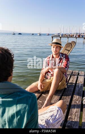 Freunden von Angesicht zu Angesicht auf hölzernen Pier neben See, Schondorf, Ammersee, Bayern, Deutschland Stockfoto