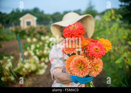 Ältere Frau mit Blumen vor Gesicht auf Bauernhof Stockfoto