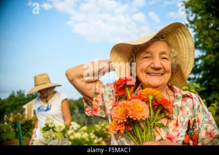 Ältere Frau festhalten Strohhut und Blumen auf Bauernhof Stockfoto