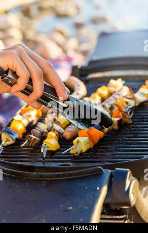 Junge mans Hand mit Zange um Würstchen und Kebab Grill Grillplatte einzuschalten Stockfoto