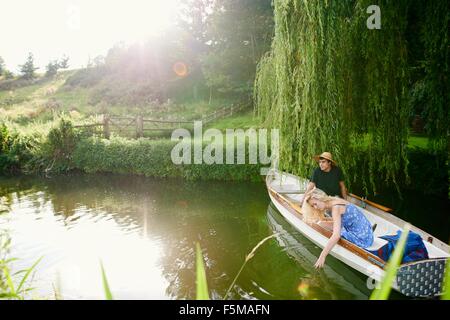 Junge Frau mit Freund berühren Wasser vom Fluss Ruderboot Stockfoto