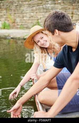 Junges Paar berühren Wasser vom Ruderboot auf ländlichen Fluss Stockfoto