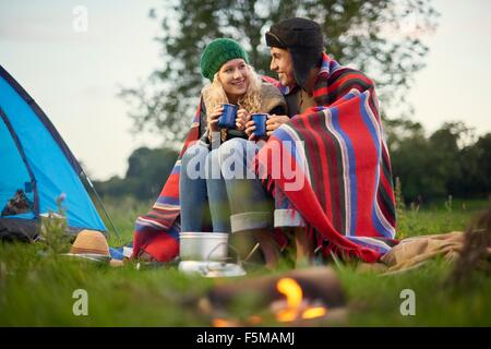 Camping Pärchen sitzen am Lagerfeuer mit Tasse Tee Stockfoto