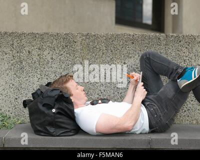 Junger Mann auf konkrete Bank liegend Schreiben von Notizen Stockfoto