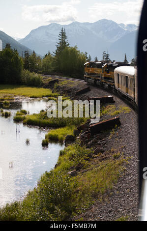 Alaska Railroad Zug von Anchorage nach Seward geht um eine Kurve mit den Bergen im Hintergrund reflektiert Weg von einem Teich Stockfoto