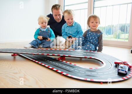 Mitte erwachsener Mann und drei Kinder mit Spielzeug spielen Rennwagen am Boden des Wohnzimmers Stockfoto