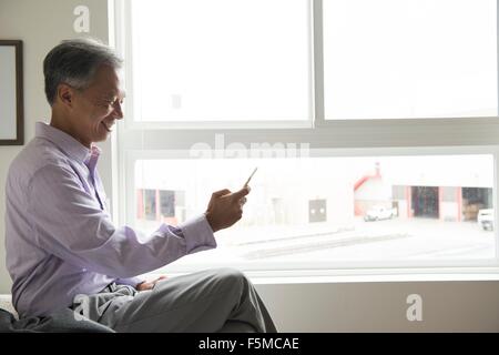 Seitenansicht des reifer Mann sitzt vor Fenster mit smartphone Stockfoto