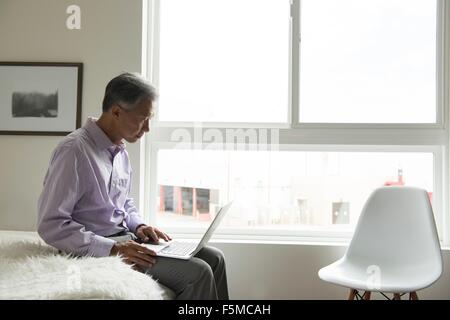 Seitenansicht der Reife Mann sitzt auf der Bettkante mit laptop Stockfoto