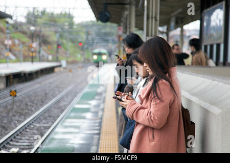 Mädchen, die Benutzung von Mobiltelefonen während des Wartens auf einen Zug, Japan Stockfoto