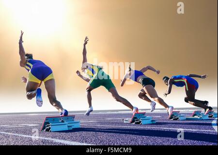 Vier weibliche Athleten auf Leichtathletik-Laufbahn verlassen Startblöcken, Rückansicht Stockfoto