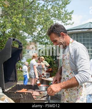 Seitenansicht des reifer Mann kochen für Familie auf Grill blickte lächelnd Stockfoto