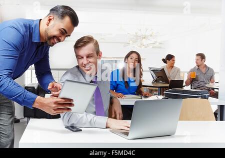 Zwei Geschäftsleute, Diskussion, Blick in die digital-Tablette, im Hintergrund arbeitenden Kolleginnen und Kollegen Stockfoto