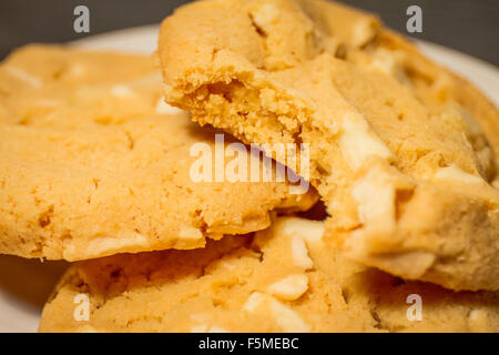 Eine Nahaufnahme der drei weiße Macadamia-Nuss Schokoladenkekse auf einem weißen Teller mit einem Biss einer entnommen. Stockfoto