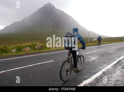 14. November 2005; Glen Coe, Schottland; Mountainbiker fahren im Regen durch Glen Coe. Glen Coe ist ein Tal in den Highlands von Schottland. Es liegt im südlichen Teil des Gebiets Lochaber Highland Council Area und gilt als Teil der traditionellen Grafschaft Argyll. Es wird oft als eines der spektakulärsten und schönsten Orte in Schottland und ist ein Teil der ausgewiesenen National Scenic Area von Ben Nevis und Glen Coe. Der Ortsname ist Glen Coe im Volksmund, aber irrtümlich, vermutlich bedeuten die "Glen des Weinens", die aufgrund der steilen Bergen möglicherweise, die drückend über die Val Turm Stockfoto