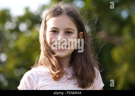 Ein junges Mädchen lächelt nach unten in die Kamera. Ihr Gesicht ist ihre feine dunkle Haare herumtanzen. Sie hat dunkle Augen und ein Lächeln. Stockfoto