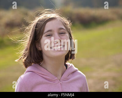 Ich bin glücklich. Ein lächelndes Mädchen elf Jahre alt, ist wieder beleuchtet von der Sonne zeigt sich ihre Fliege entfernt Haare. Stockfoto