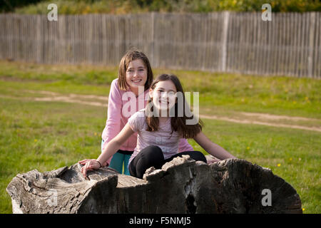 Zwei Mädchen spielen vorgeben. Zwei Mädchen spielen auf einem Baumstamm im Park so tun. Sie sind für die Kamera durchführen. Stockfoto