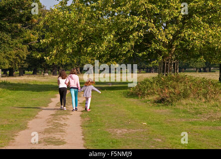 Drei junge Mädchen sind aus einen großen Park zu erkunden. Die zwei älteren zu Fuß Arm im Arm, während die älteste die Hand der jüngeren hält. Stockfoto