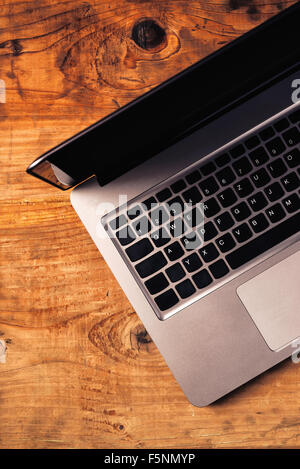 Laptop auf rustikalen hölzernen Schreibtisch, getönten Retro Bild mit leere Kopie Raum. Draufsicht von gebürstetem Metall Computer Körper mit schwarz Stockfoto