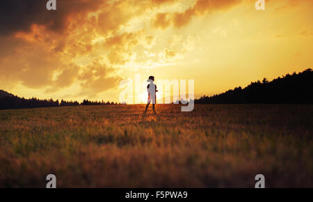 Silhouette eines glücklichen Kindes spielen auf der Wiese bei Sonnenuntergang Stockfoto