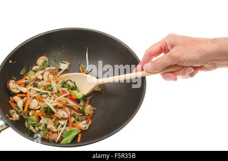 Hand mit Holzlöffel rühren Huhn und unter Rühren braten Gemüse im Wok vor einem weißen Hintergrund Stockfoto