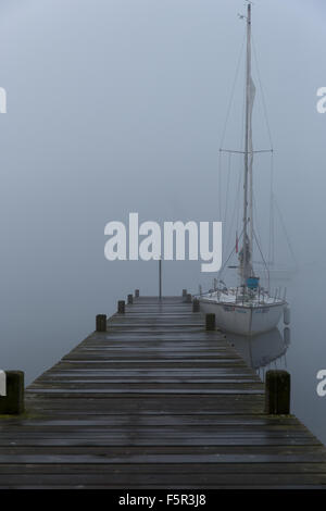 Yachten ankern neben einem Holzsteg im Nebel am Lake Windermere in Ambleside Stockfoto