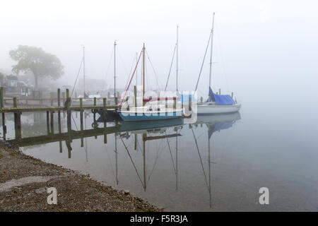 Yachten ankern neben einem Holzsteg im Nebel am Lake Windermere in Ambleside Stockfoto