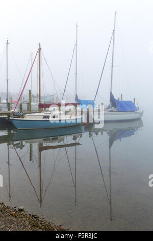 Yachten ankern neben einem Holzsteg im Nebel am Lake Windermere in Ambleside Stockfoto