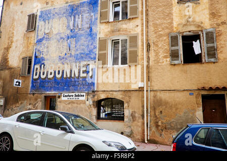 Die Straßen von Aups, Frankreich. Straße mit Autos, alte Dubonnet Werbung, Couture und Hemd im Fenster. Stockfoto