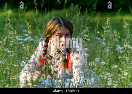 Junges Mädchen, das im Gras sitzt und Blumen in Meadow Daisies Frühling Mai Meadow Südmähren Traditionen Mährisches Folklore Kostüm weibliches Volkskleid pflückt Stockfoto