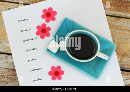 Tasse Kaffee und Wochentagen geschrieben auf weißem Papier und bunte Blumen Stockfoto