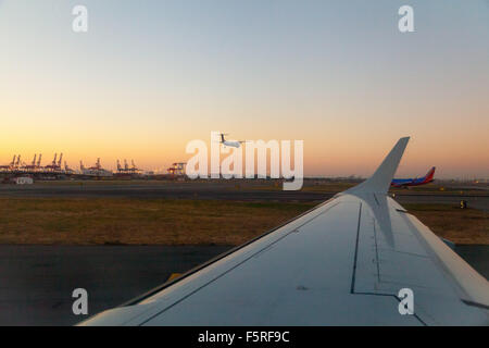 Blick aus dem Flugzeugfenster über die Flügel des Flugzeugs zu sehen, ein anderes Flugzeug Landung, bei Sonnenaufgang am Flughafen Newark. Stockfoto