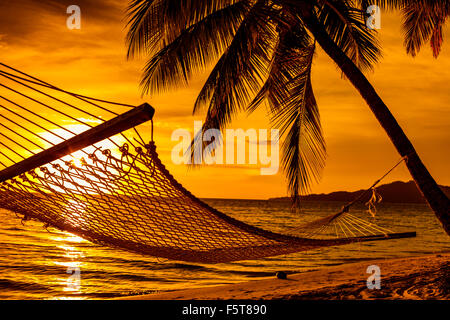 Silhouette der Hängematte und Palmen an einem tropischen Strand bei Sonnenuntergang Stockfoto