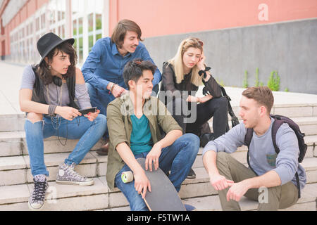 Gruppe junger multiethnischen Freunde sitzt auf einer Treppe im Gespräch miteinander, mit Skateboard, Spaß - Freundschaft, entspannende Konzept Stockfoto