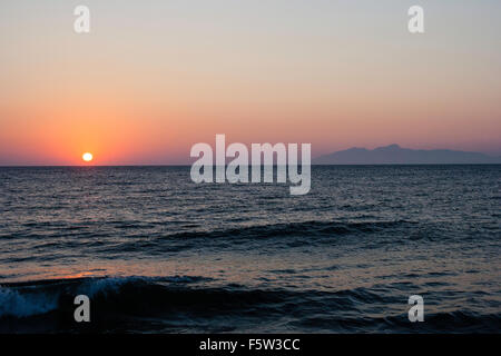 Sonnenaufgang und Roter Himmel über das Meer mit der Insel Anafi, teils durch frühe Morgen Dunst versteckt. Vom Kamari Beach Resort auf Santorin gesehen. Stockfoto