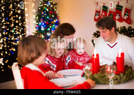 Große Familie mit drei Kindern zu Hause Weihnachten zu feiern. Festliches Abendessen am Kamin und Weihnachtsbaum. Eltern und Kinder essen Stockfoto