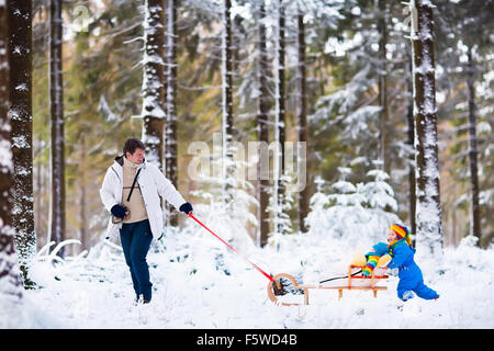 Vater und Kinder genießen Schlittenfahrt im Winterwald. Baby Boy und Kleinkind Mädchen Schlitten im verschneiten Park. Papa ziehen Kinder auf Schlitten Stockfoto