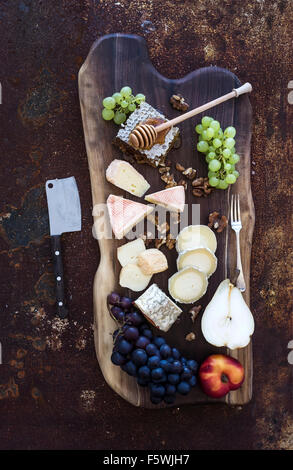 Wein-Aperitif-Set: Französische Käse-Auswahl, Waben, Trauben, Pfirsich und Walnüsse auf rustikalem Holzbrett über dunkle Grunge Metall Stockfoto