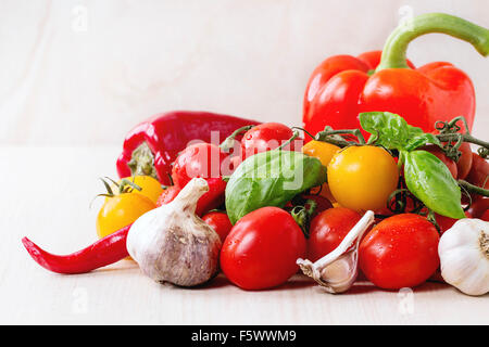 Auswahl an bunten Cherry-Tomaten mit Pfeffer, Knoblauch und Basi über weiße Holzoberfläche Stockfoto