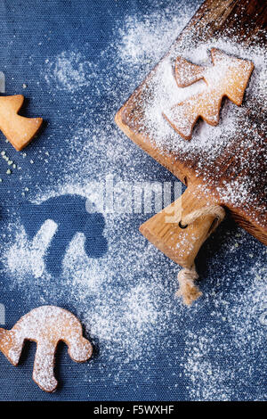 Weihnachten Spritzgebäck für Tassen Puderzucker und kleine Schneidebrett über Tisch mit blauen Tischdecke. Ansicht von oben. Form einer Stockfoto