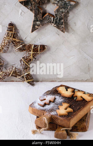 Weihnachten Spritzgebäck für Tassen in Zuckerpuder auf kleine Schneidebrett über Tisch mit weißer Tischdecke. Weihnachts-Dekor ein Stockfoto