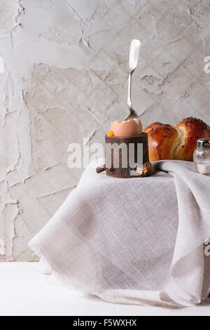 Frühstück mit fing an zu essen wachsweiches Ei mit strömenden Eigelb in hölzernen Eierbecher und hausgemachtem Brot mit Salz und Silber Stockfoto