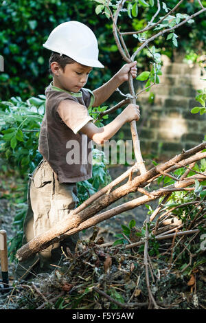 Junge kaukasier Kind, Junge, 8 Jahre alt, im Garten kämpfen zu ziehen und ein großer Zweig von Schnitt- Baum beim Tragen weiße harte Sicherheit - hat. Stockfoto