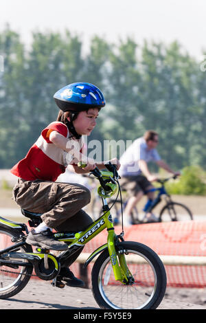 Seitenansicht der Kaukasischen 9 Jahre altes Kind, Junge, Reiten Fahrrad des Kindes bei der Geschwindigkeit mit aufgeregten Mimik. Trägt blaue Helm und T-Shirt. Stockfoto