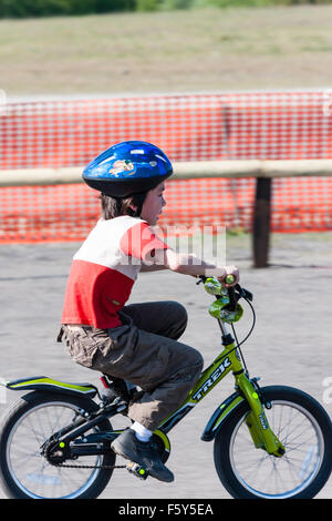 Seitenansicht der Kaukasischen 9 Jahre altes Kind, Junge, Reiten Fahrrad des Kindes bei der Geschwindigkeit mit aufgeregten Mimik. Trägt blaue Helm und T-Shirt. Stockfoto