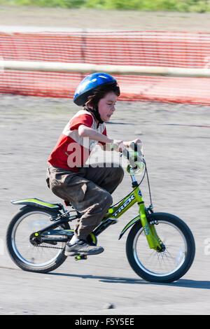 Seitenansicht der Kaukasischen 9 Jahre altes Kind, Junge, Reiten Fahrrad des Kindes bei der Geschwindigkeit mit aufgeregten Mimik. Trägt blaue Helm und T-Shirt. Stockfoto